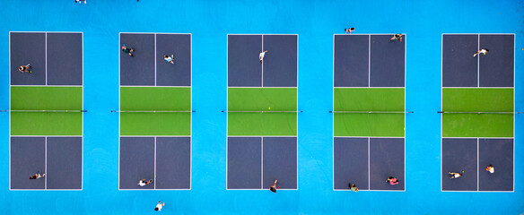 Aerial view of multiple pickleball courts with players in action. Colorful blue and green outdoor sports complex on a sunny day. Recreational activity and healthy lifestyle concept