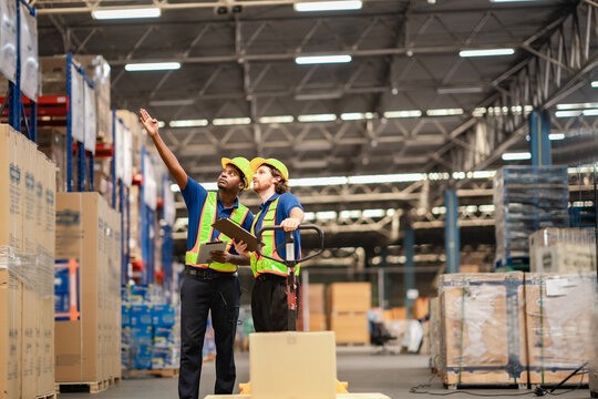 White and black co-worker have conversation about work flow at aisel wth warehouse background behide.