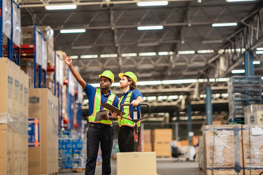 Discussion about machinery layout and traffic paths guided by digital tablet in busy warehouse.