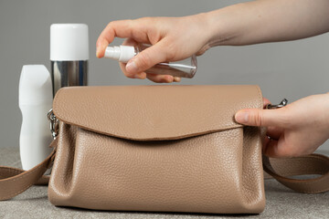 Care of leather products. Applying a special spray of the product to the surface of a leather handbag.