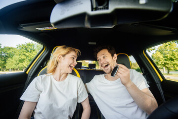 Happy woman and man riding in a car for a romantic vacation, chatting and laughing while enjoying...