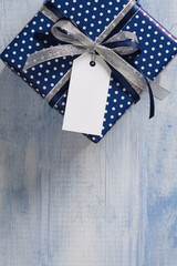 The blue gift box is tied with a silver-dark blue ribbon. An empty white tag hangs from the bow, on...
