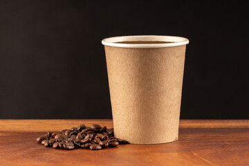 Disposable coffee glass with natural coffee beans on a black and wooden background