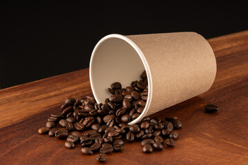 Disposable coffee glass or cup with natural coffee beans on a black and wooden background 