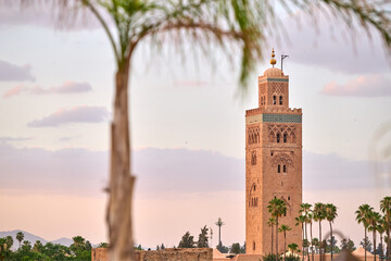 Obraz premium Koutoubia Mosque with its iconic minaret at dusk in Marrakech. Ancient architecture surrounded by palm trees. Scenic view of cultural landmarks and historical sites.