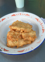 Mendoan, a popular Indonesian snack, features thinly sliced tempeh coated in seasoned batter and fried to golden crispiness, offering a savory, crunchy treat enjoyed with spicy dipping sauce.