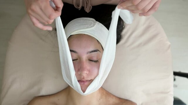 Esthetician applying gauze to a client's face during a hydrafacial treatment, slow motion overhead shot