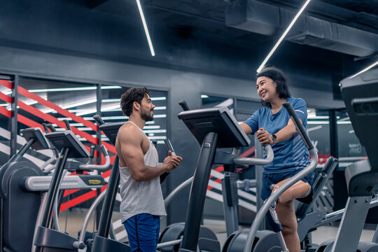 active middle aged woman,a person with prosthetic leg talking to trainer while exercise on gym equipment in fitness club - Powered by Adobe