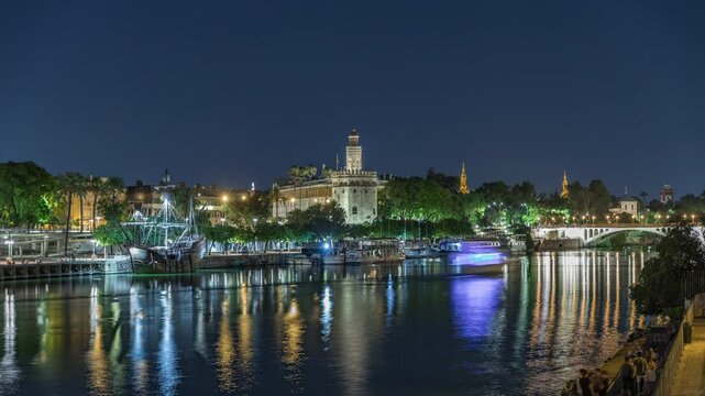 Torre del Oro watchtower in Seville, Spain. Day to night transition timelapse with city lights reflecting on water and scenic aerial view of waterfront. Tour boat floating along the Guadalquivir River
