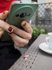Woman sitting at cafe, working on smartphone with unique circular camera bump, coffee and empty...