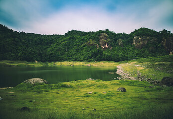 A peaceful mountain with a lake reflecting the green forest and cloudy sky creates a stunning...