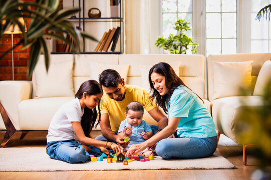 Playing with wooden toys, Indian infant enjoys bonding time with sister and parents indoors