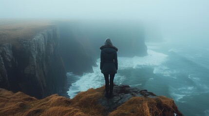 A person stands on the edge of a cliff, shrouded in mist, gazing at the ocean waves below, evoking feelings of solitude and introspection in nature's embrace.