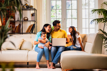 Young family using laptop indoors on sofa for shopping, surfing, and spending time together happily