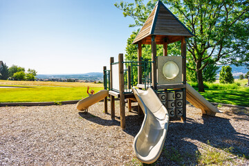 A young boy slides on outdoor children's playground equipment at a small park overlooking a city during summer.