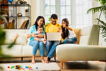Attending video call Indian family waves sitting on sofa with daughter and baby indoors