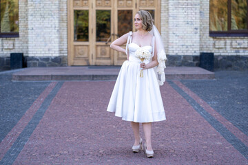 full length portrait of beautiful young bride in white short wedding dress and veil. Bride holding...