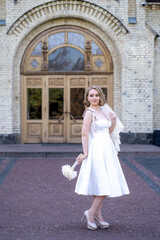 Fototapeta premium full length portrait of beautiful young bride in white short wedding dress and veil. Bride holding bouquet of dried flowers. Wedding day