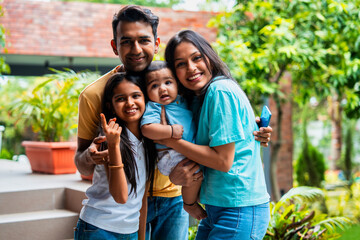 Indian parents with infant and daughter posing in park while smiling close together lovingly