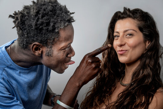 Playful man booping his partner's nose with a goofy face while woman smirks at the camera.
