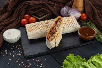 Shawarma, Kebab, Doner in lavash with fresh vegetables on a black tray with two sauces