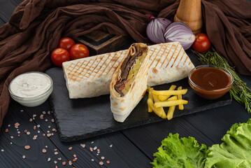 Shawarma, Kebab, Doner in lavash with fresh vegetables on a black tray with two sauces