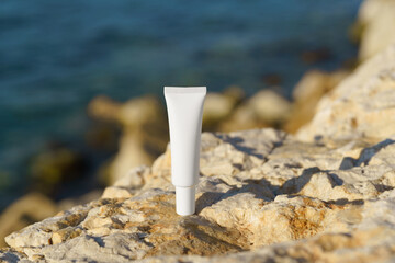 Minimalist white mockup cream or lotion tube on rocky shore with ocean view. Perfect for beauty, skincare, or sunscreen with spf and natural product branding.
