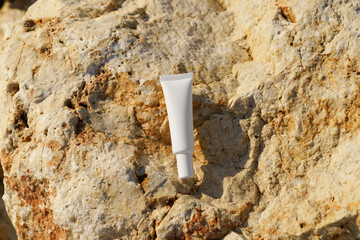 White thin tube of eye cream on limestone rock illuminated by the sun. Concept of sensitive and...