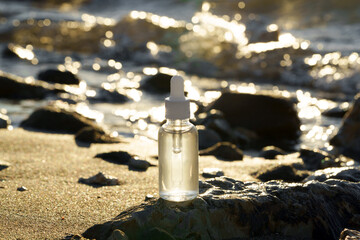 Natural facial serum in glass dropper bottle on beach stones. Background of waves and sea suggests clean beauty, SPF protection, and deep skin nourishment.
