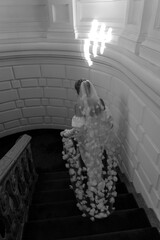 The black and white image captures a bride descending a grand staircase, showcasing her elegant...