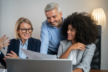 Three busy happy middle aged professional business man and two women executive leaders team using laptop working on computer at work desk having conversation on financial project at meeting in office.