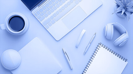 Modern workspace featuring a laptop, coffee cup, headphones, notebook, and stationery items arranged on a blue background, creating an organized and inspiring environment for productivity
