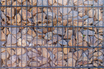 A detailed view of a wall made of irregularly shaped rocks secured within a black metal grid. The...
