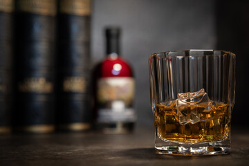 Close-up of whisky glass with ice, bottle and books blurred in background