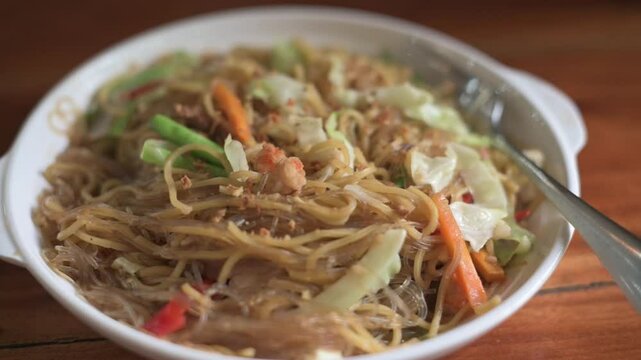 Vertical screen showing vibrant pancit bihon noodles in Bohol, Philippines, topped with sliced vegetables