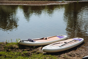 Two vibrant StandUp Paddleboards rest on the sandy shore of a tranquil river, inviting adventurers to explore the shimmering water and enjoy invigorating exercise in natures beauty