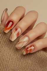 Elegant autumnal nail art: Hand with oval-shaped nails, featuring a geometric design in shades of brown, orange and cream, with gold line details. Ideal for beauty themes, autumn, manicure trends and 