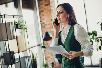 Confident businesswoman on the phone in modern office holding documents showcasing professionalism...