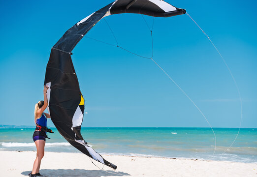 Young woman kitesurfing teacher holding a kite on a beach, water sports, activities. Kitesurfing school camp in Egypt