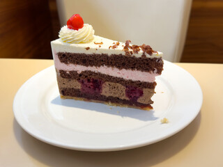 Slice of black forest cake with cream and cherry on plate