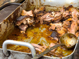 Juicy shredded pork in a rustic metal pan with seasoning and juices