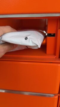 Hand retrieving parcel from orange self-service parcel locker &mdash; modern contactless delivery and online shopping pickup concept
