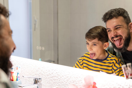 Father and son showing tongue on bathroom mirror