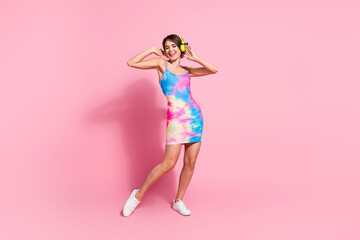 Young woman in colorful summer dress posing against pink background, exuding joy and confidence.