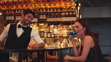 Sitting in smiling beautiful woman guest lively taking with smart bartender while drinking mixed...
