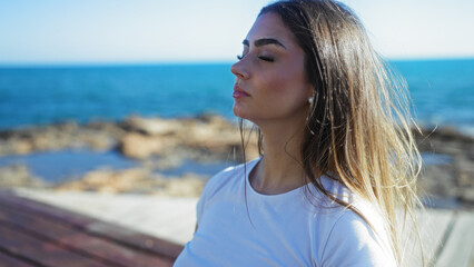 Woman meditating peacefully on seaside promenade with eyes closed, soaking in ocean breeze under...