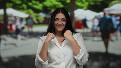 Fototapeta premium Woman boxing confidently on a sunny city street, showcasing strength and empowerment amidst an outdoor urban setting with blurred pedestrians in the background.