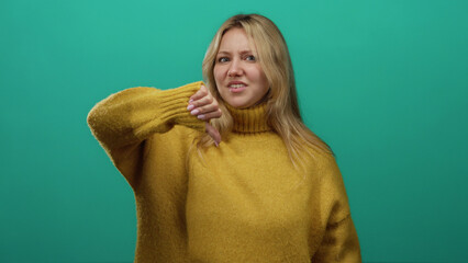 Woman expressing dislike wearing yellow sweater with thumbs down against vibrant green background...