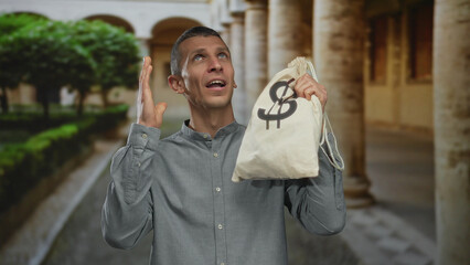 Man holding money bag with dollar symbol looking surprised on a street with a picturesque...