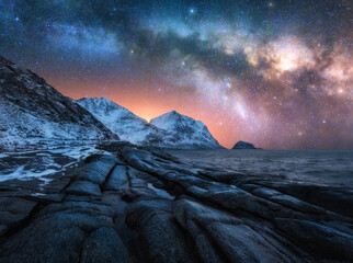 Night starry sky with glowing Milky Way, rocky shore with stones in water. Winter colorful...